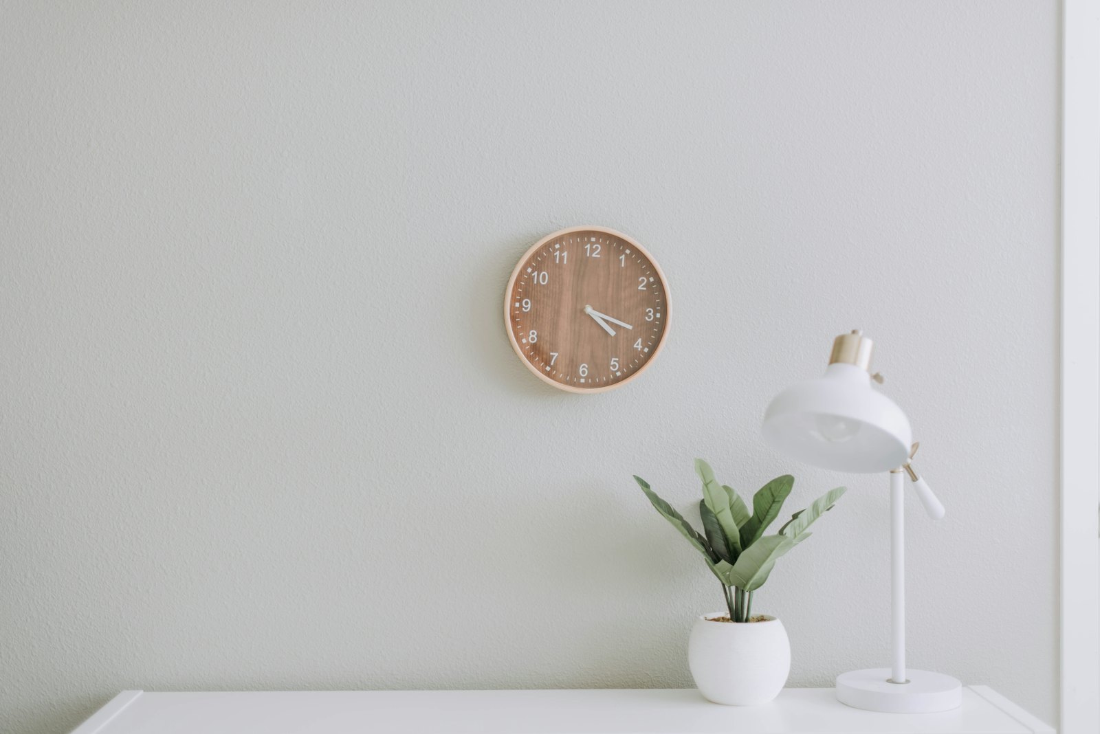 Minimal white desk with a wall clock, white lamp and small plant, styled in the spirit of Alessi design