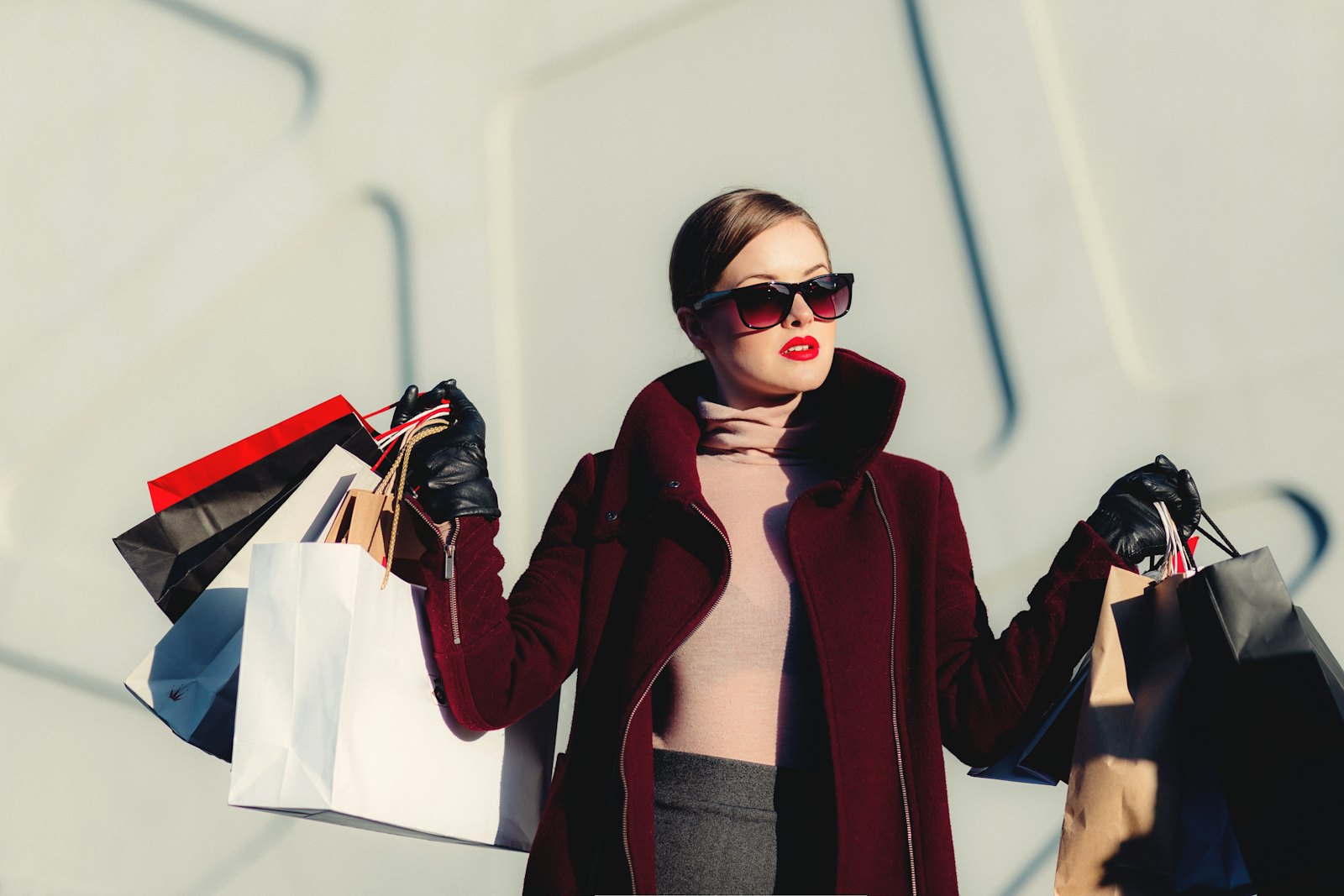 Stylish woman in sunglasses and a burgundy coat holding shopping bags, channelling the spirit of Carine Roitfeld Irreverent