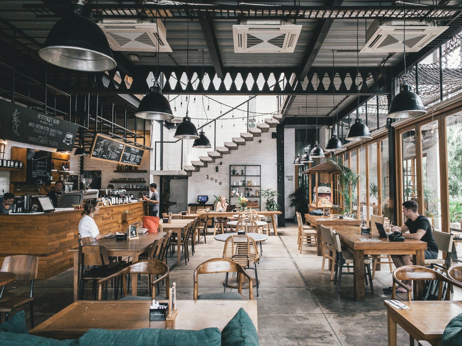 Large industrial-style restaurant with long wooden tables and pendant lights, typical of east London hotspots