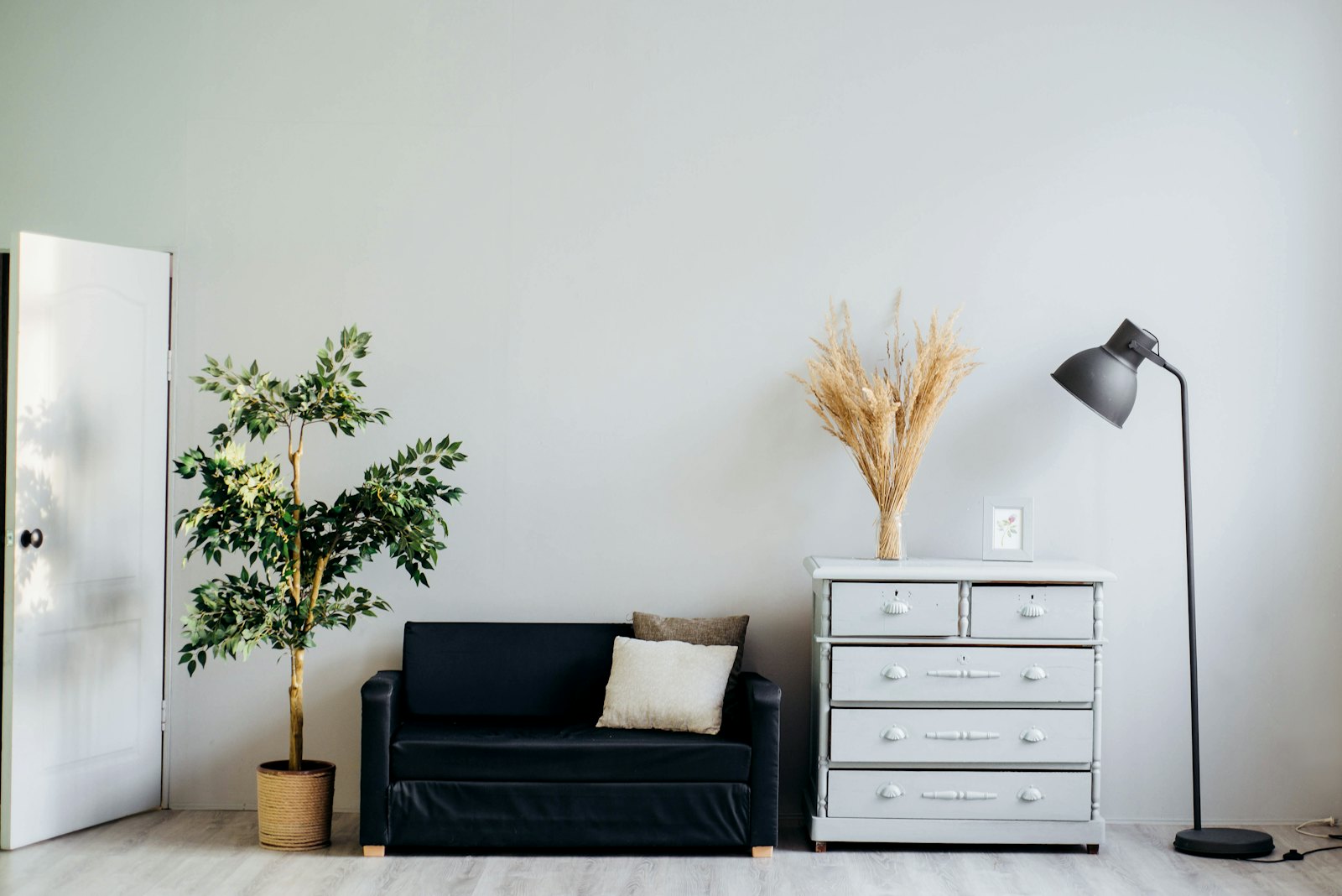 Calm, decluttered white room with a black sofa, chest of drawers and floor lamp
