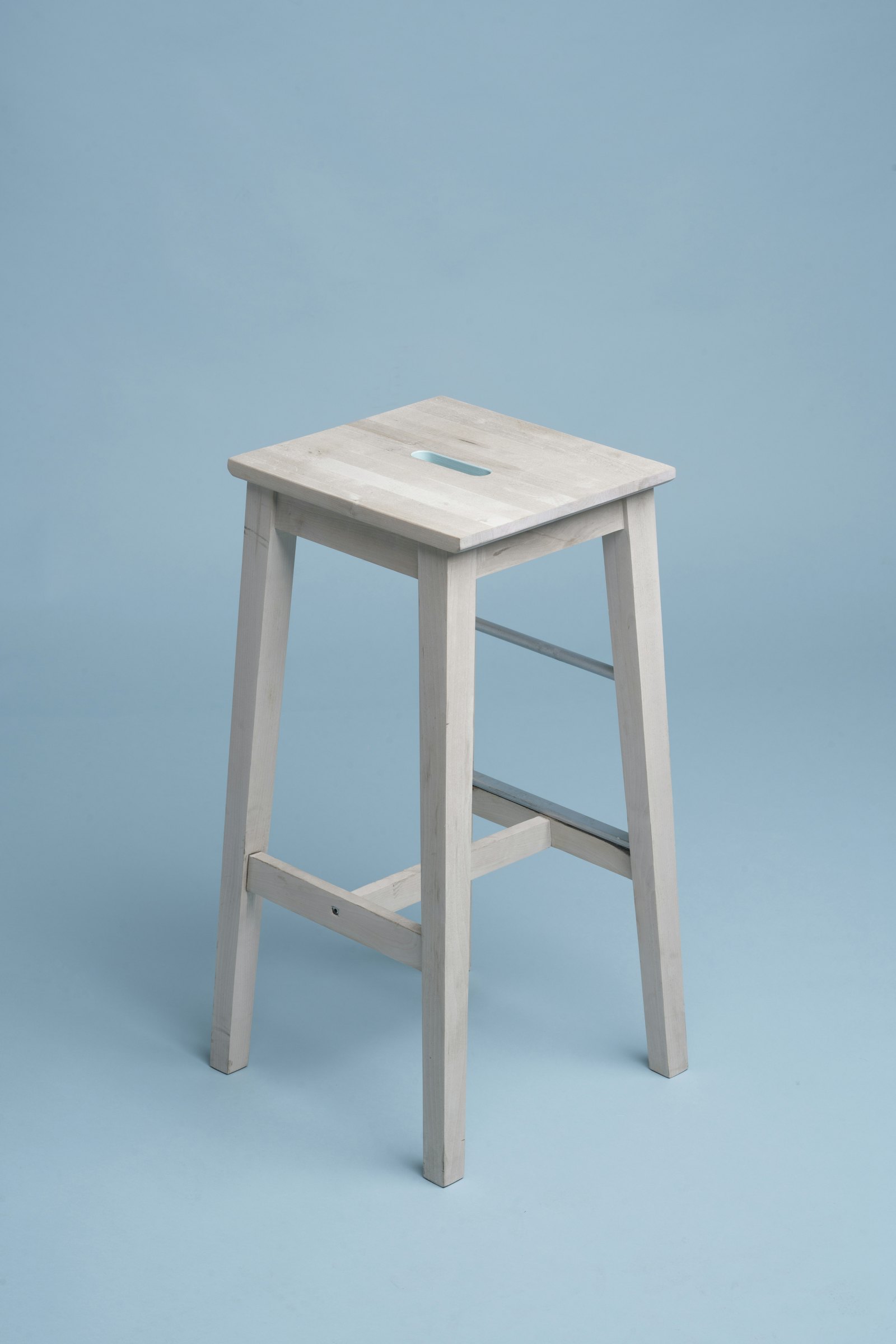 Simple pale wooden stool from Made by Jason photographed against a bright blue background