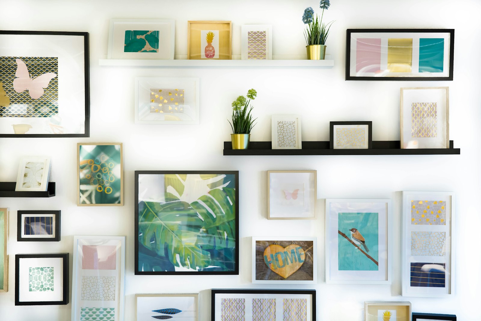 White wall with floating picture ledges holding many framed colourful limited edition prints