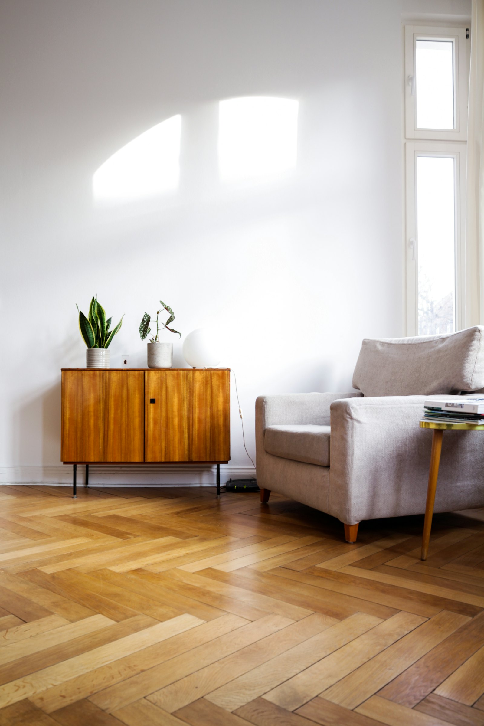 Sunny hallway with herringbone floor, armchair and sideboard