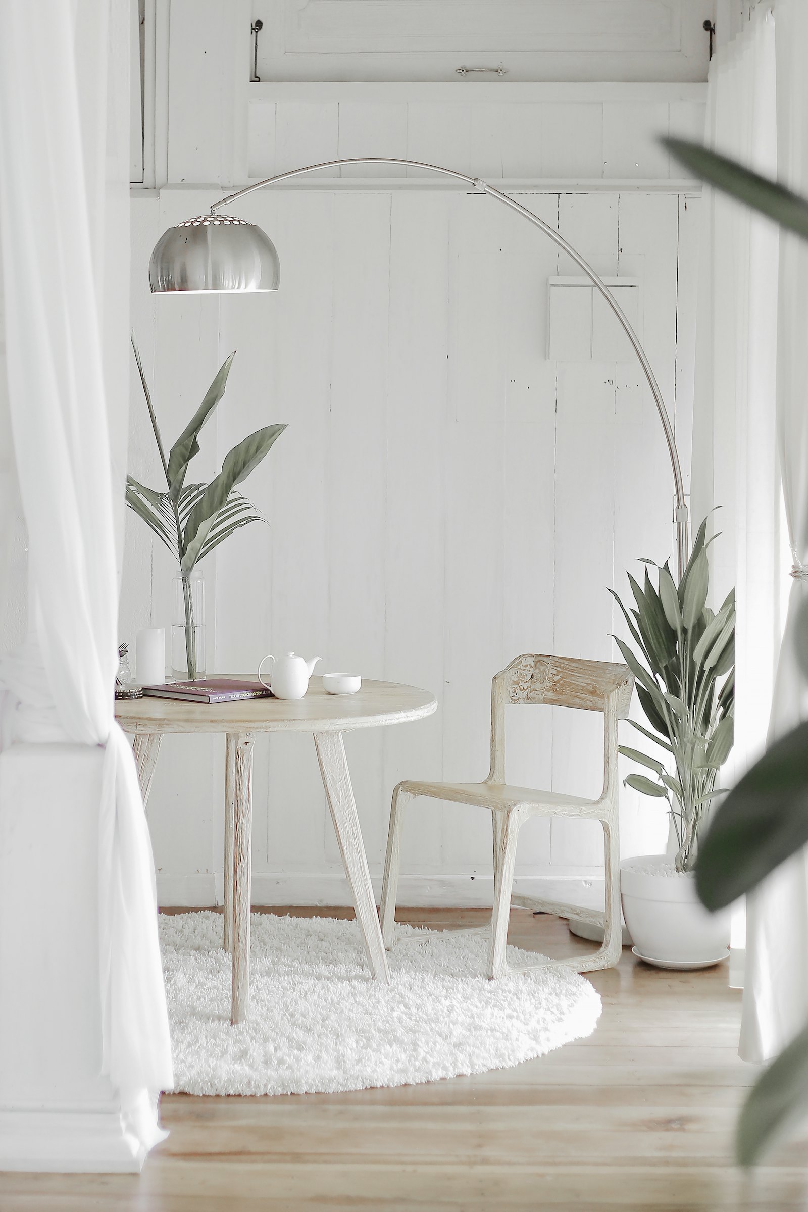 White Scandinavian corner with an arc lamp, white table and chair and green plants, showing Swedish interior style