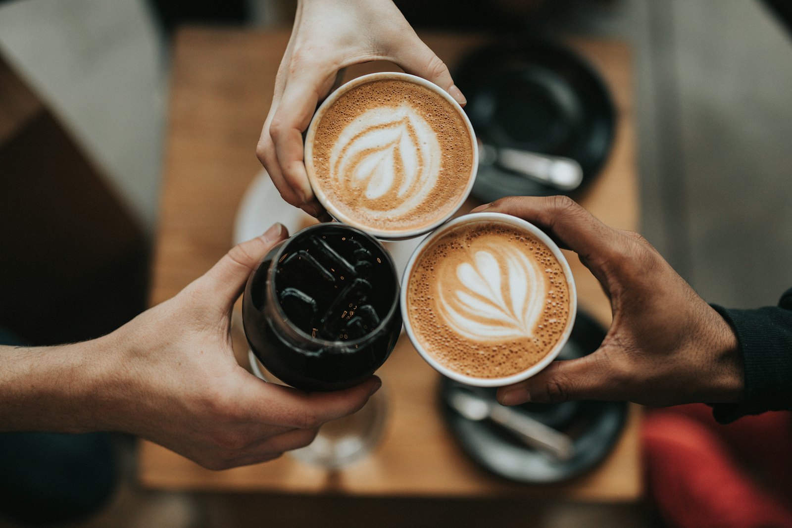 Hands clinking two cups of latte art coffee, a small everyday pleasure taken seriously